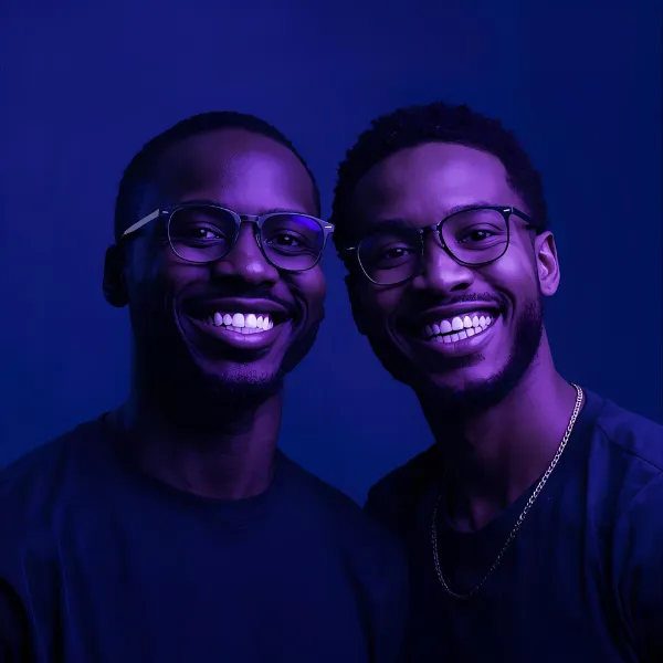 Two men wearing glasses smiling directly at the camera, illuminated with deep blue and purple lighting.