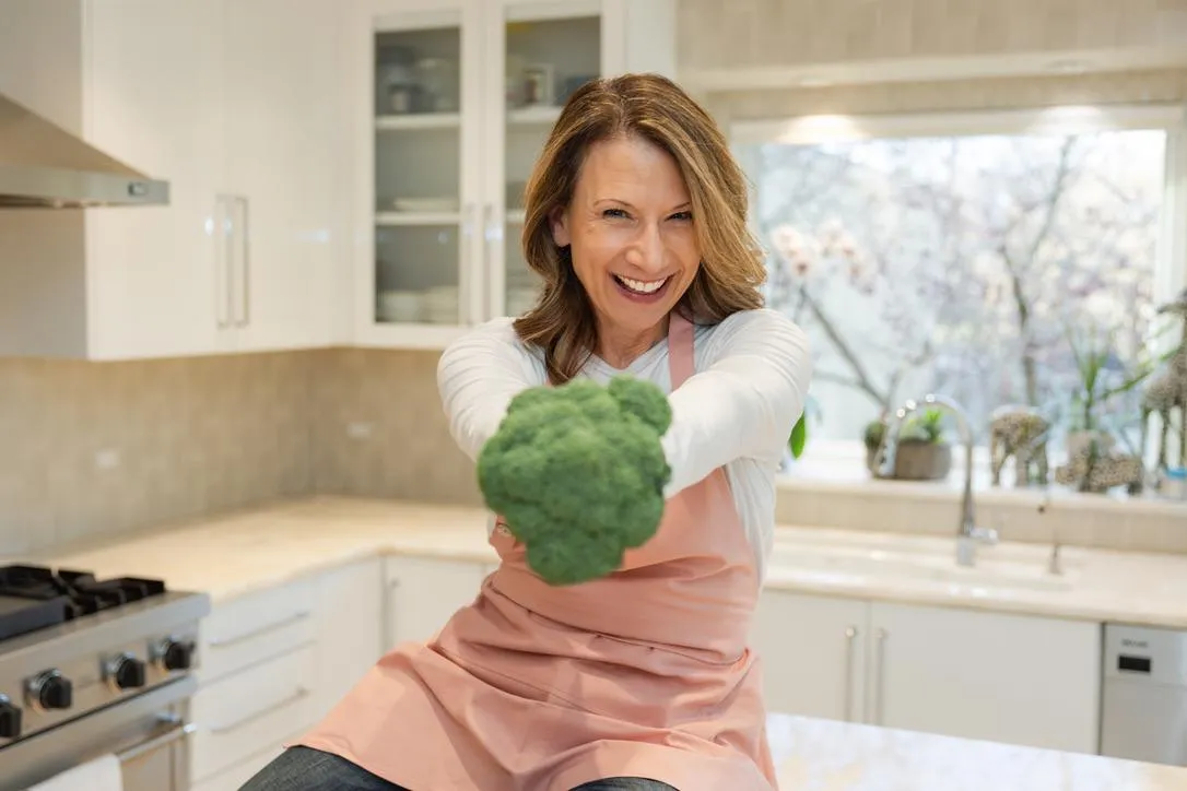 Certified health coach and movement specialist sitting on wooden stairs in a bright home, wearing a purple sleeveless top and jeans, representing strength, mobility, and wellness