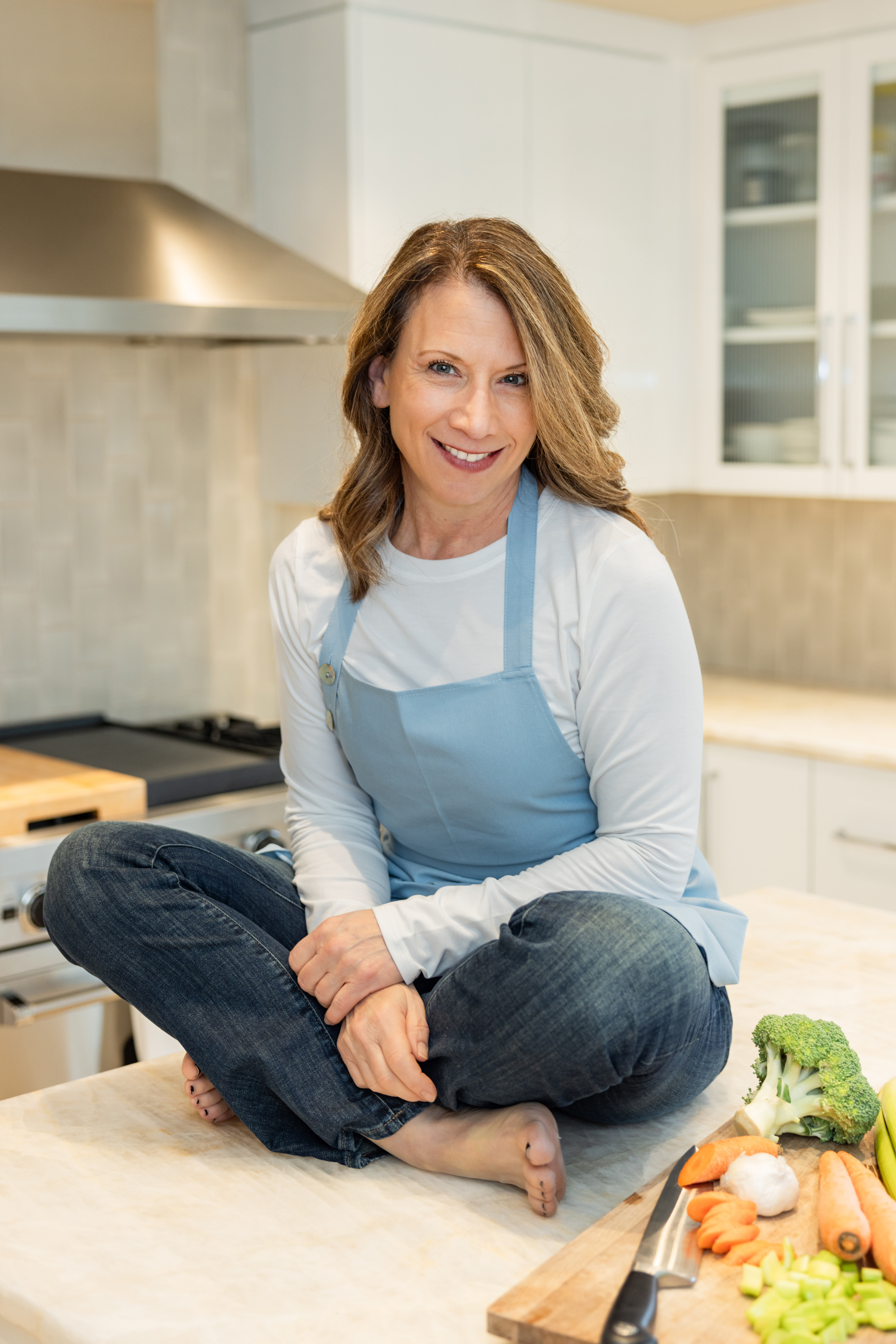 Maria Rigo seated at the top of the table smiling with some vegetables on the side