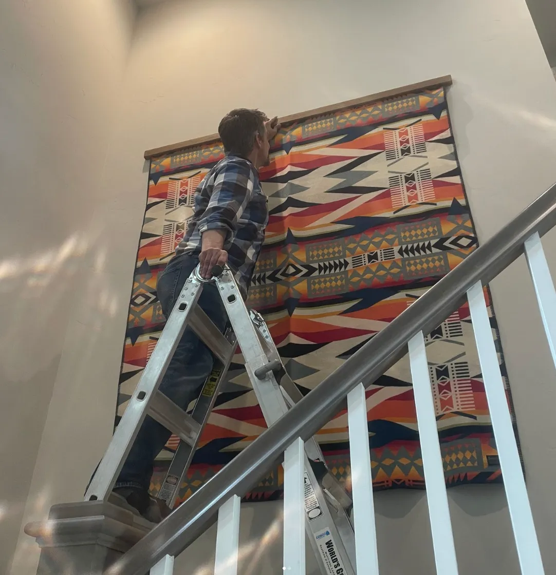 Large artwork installation project using ladder access for oversized artwork placement in a residential stairwell