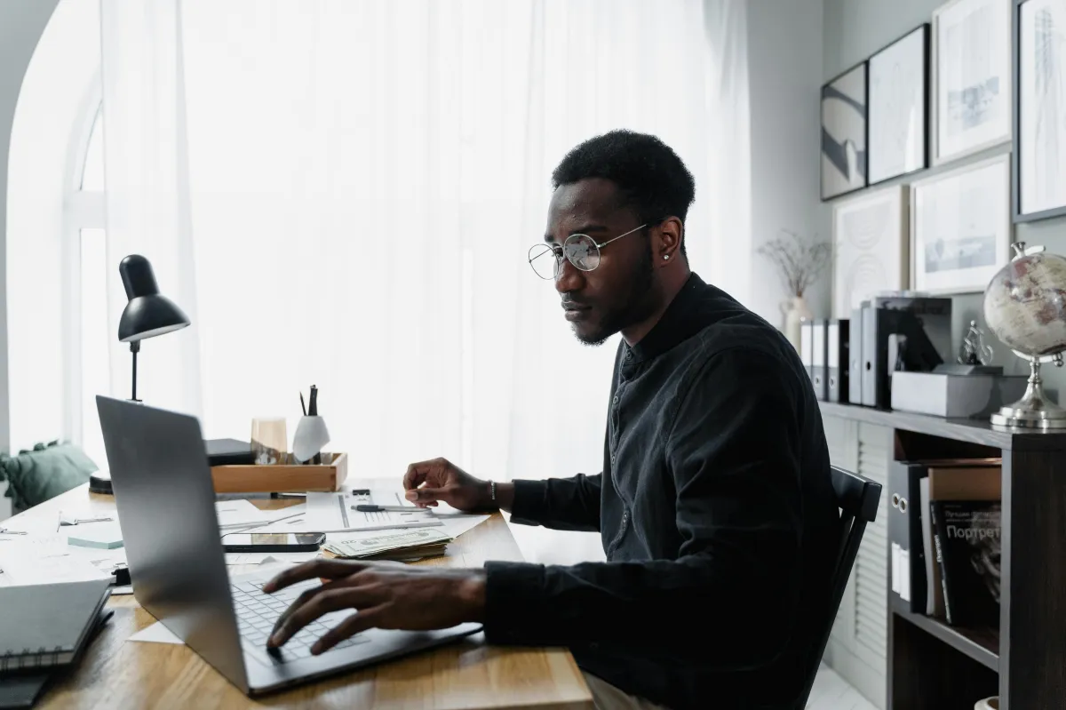 Professional black man, man with glasses, man wearing all black at laptop