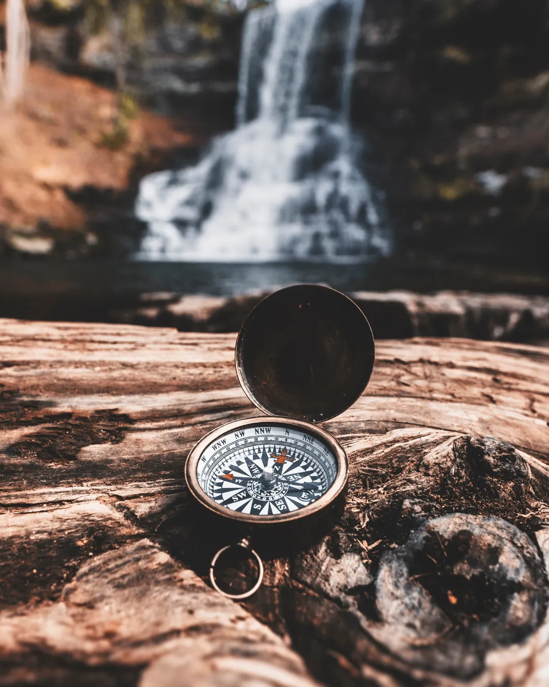 Open compass sitting on wood with a waterfall in the background