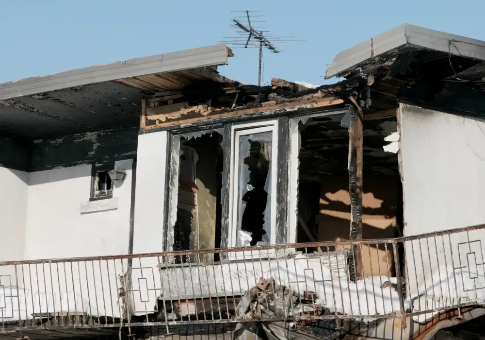 Fire-damaged home with burned exterior walls, roof, and windows.