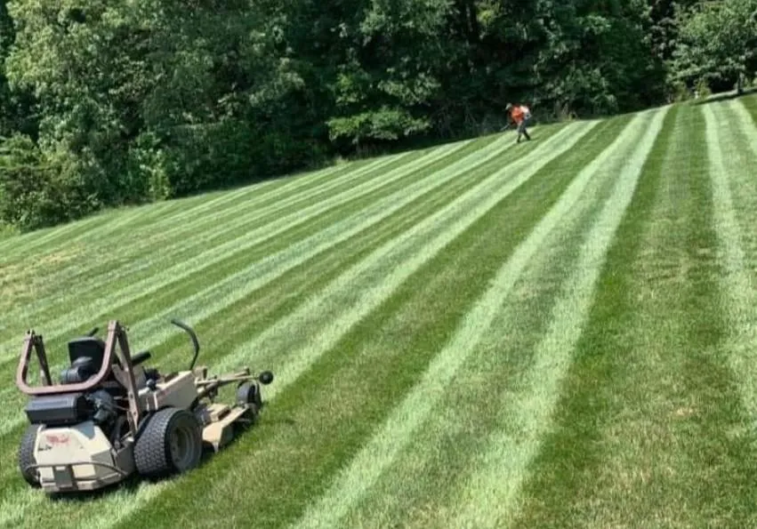 Freshly mowed commercial lawn with visible stripe cuts and riding mower parked nearby