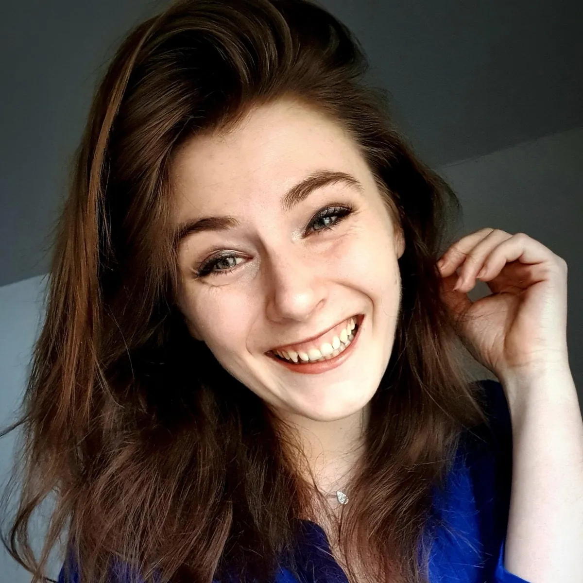 Chiara Wakeley, a smiling woman with long brown hair, wearing a blue top, and social media coordinator of Inclusive Change, posing in a friendly and approachable manner.