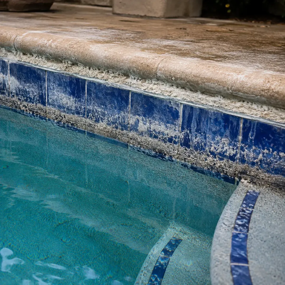 Heavy white calcium and mineral deposits along the tile and coping of a hard-water swimming pool.