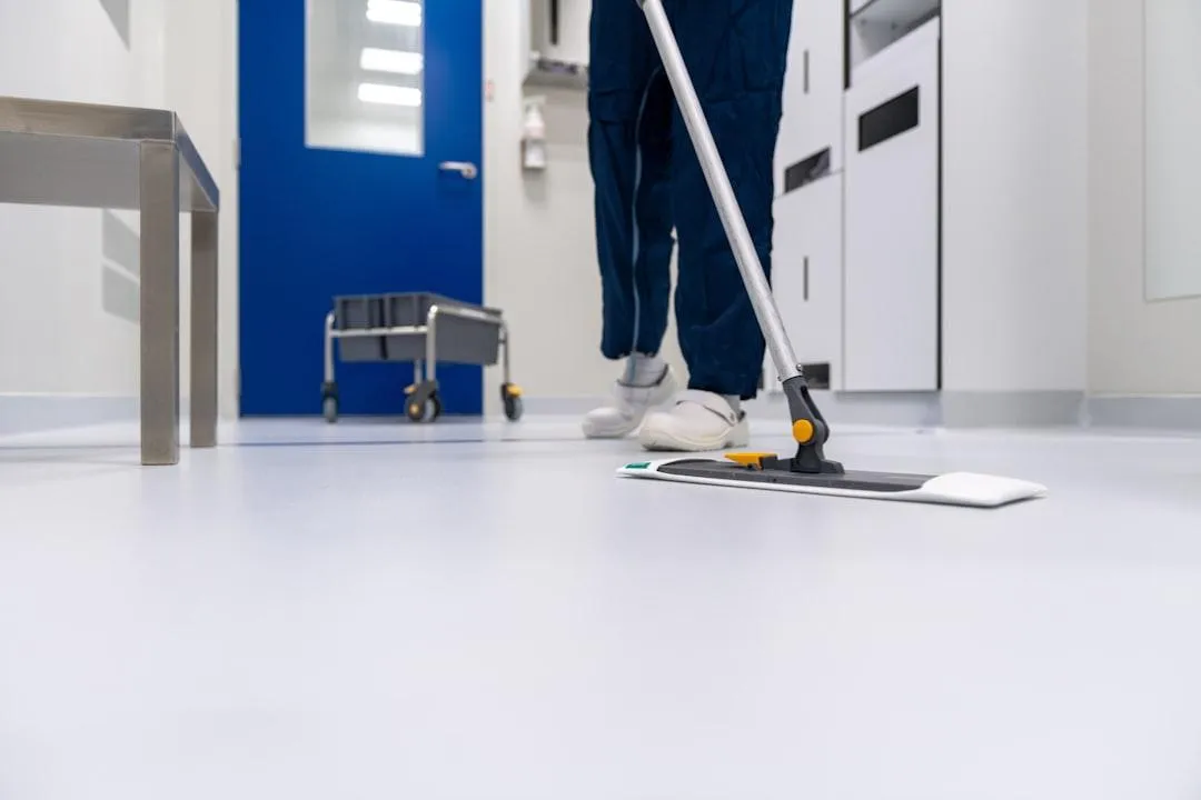 a woman in a green shirt and black gloves vacuuming a gray ottoman