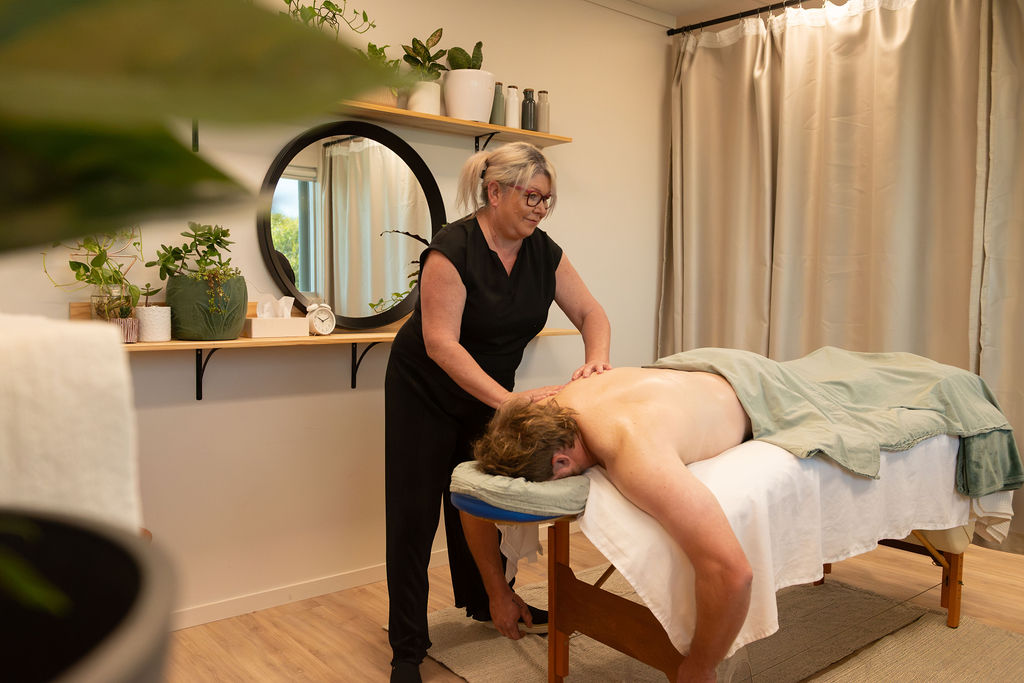 Massage therapist giving a relaxation massage to a client on a table in a room with plants and a round mirror.