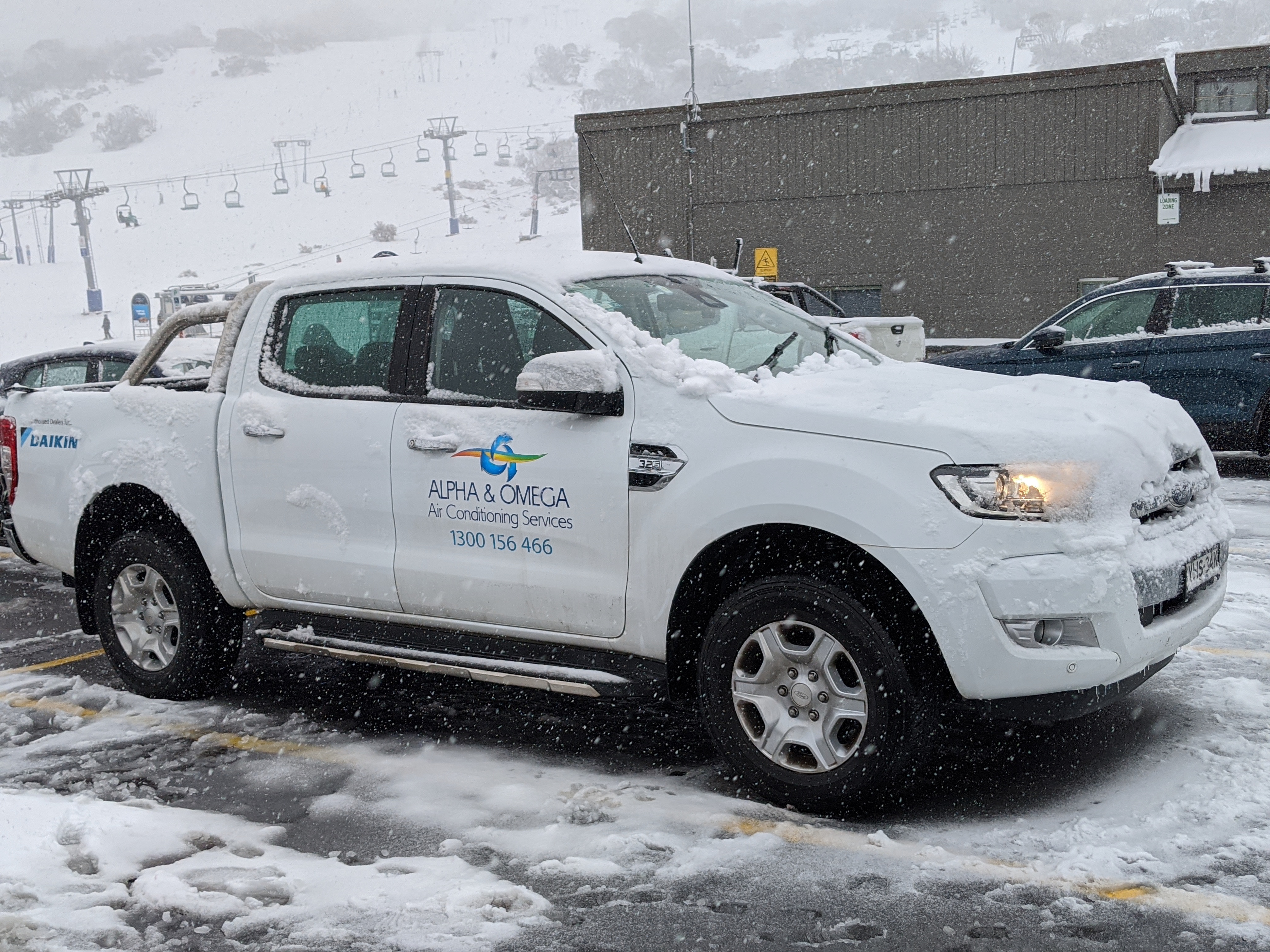 White Alpha & Omega branded service utility truck covered in snow, parked outdoors in a snowy environment.