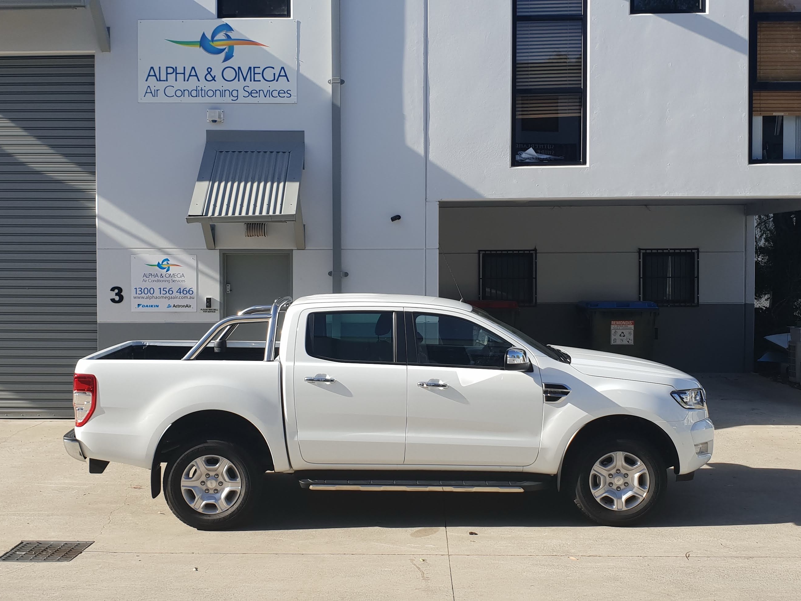 White pickup truck with Alpha & Omega branding parked outside a multi-story building