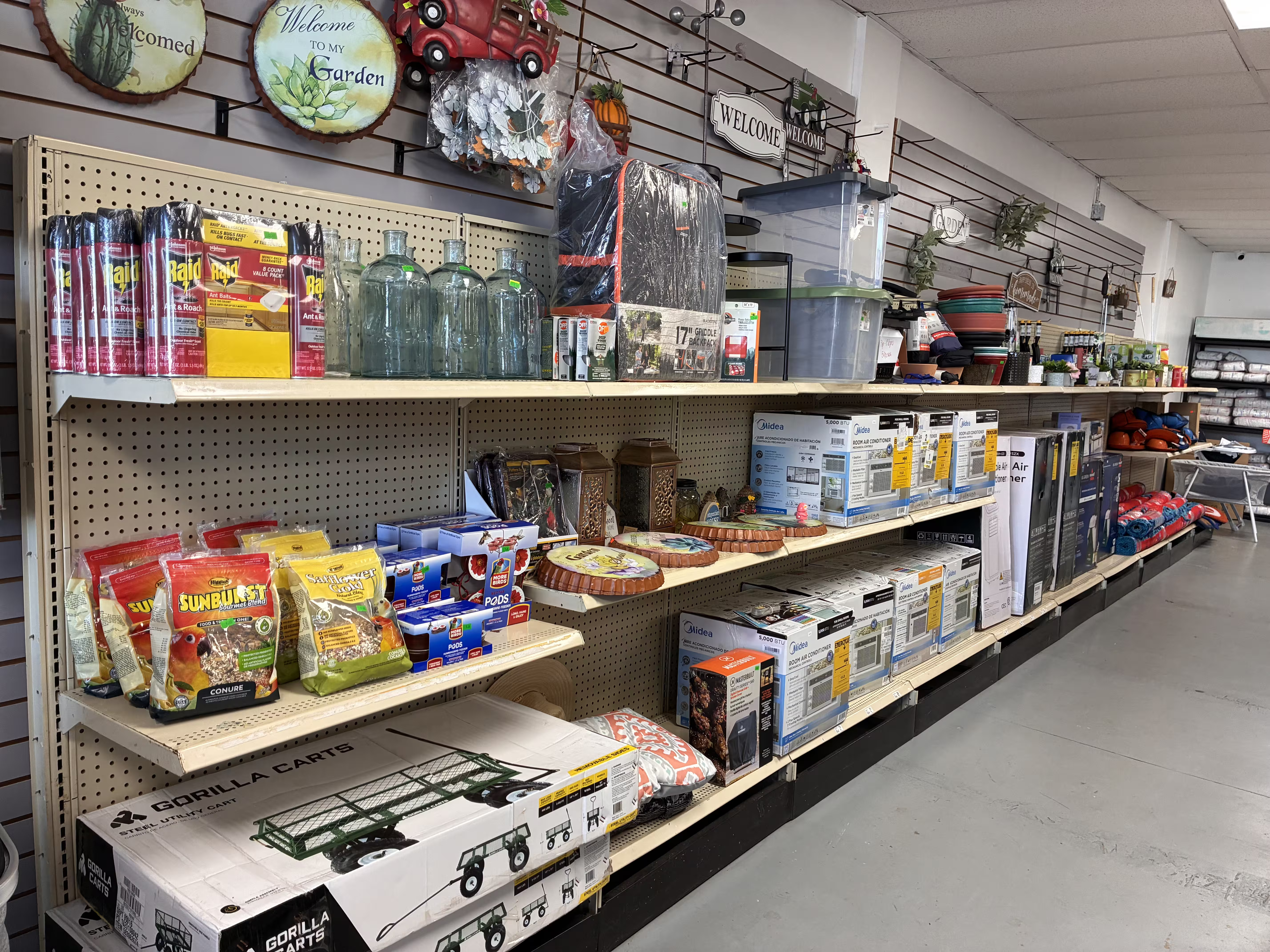 Long retail toy aisle with multiple shelves filled with colorful boxed toys, including action figures, superhero characters, toy trucks, dolls, playsets, building blocks, and educational toy kits, neatly organized under bright store lighting with a clear walkway on the right side.