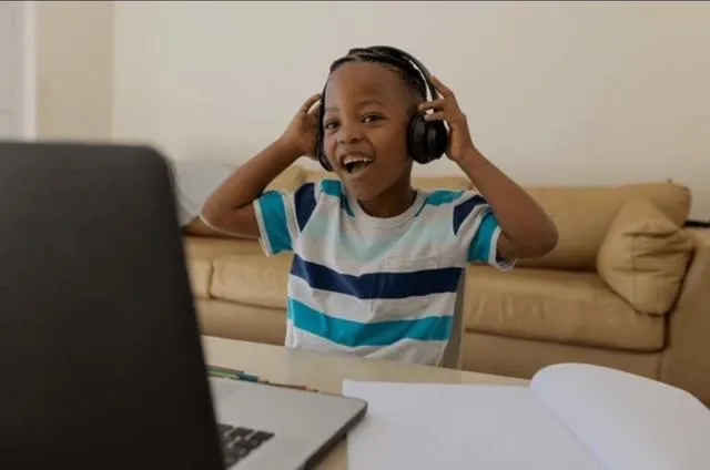 Child with headset smiles as he engages with laptop