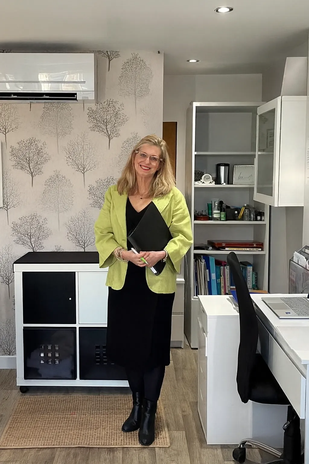 Carrie Vogel-Dennett standing in front of a bookshelf filled with coaching and psychology books, wearing professional attire, exuding confidence and warmth. The setting is a well-lit, inviting office, with certificates and awards subtly visible in the background.