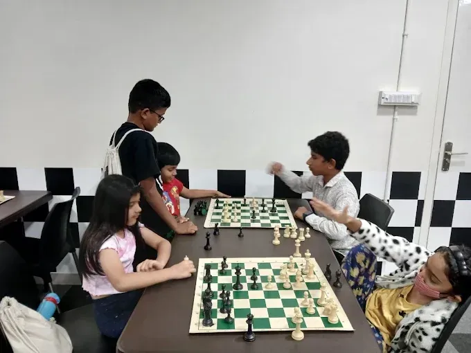 Children playing chess at a table indoors, with chessboards set up