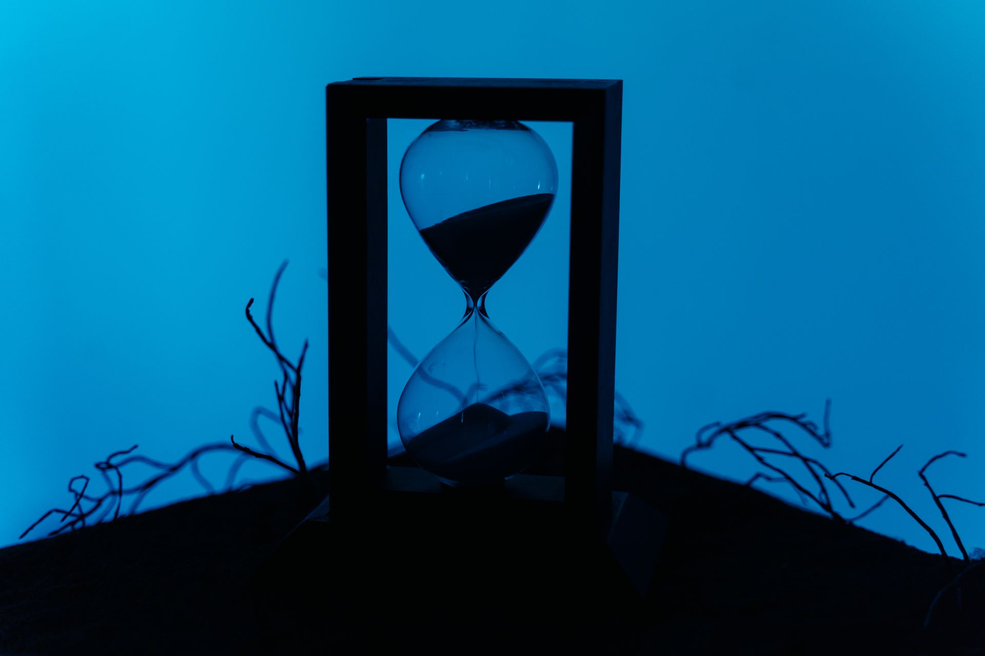 A silhouette of an hourglass set against a vivid blue background, highlighting the passage of time by Ron Lach