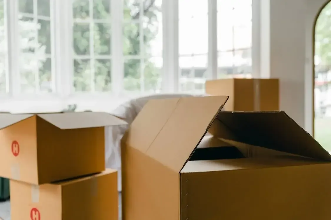 Open cardboard boxes in a room with large windows, suggesting moving or unpacking.