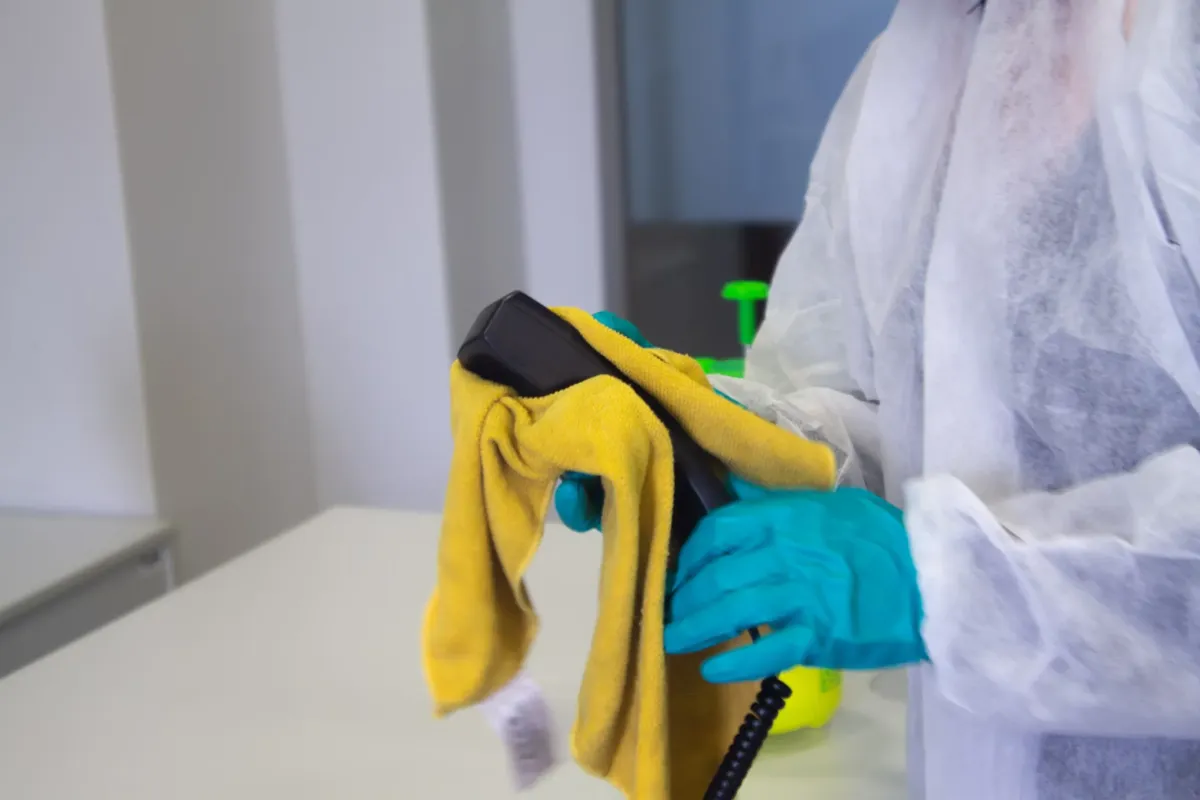 Person in protective gear wiping a surface with a yellow cloth.