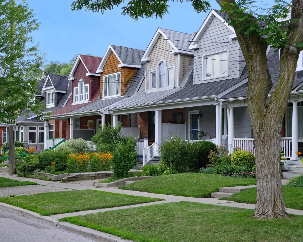 Row of colorful suburban houses with front porches and a tree-lined street.