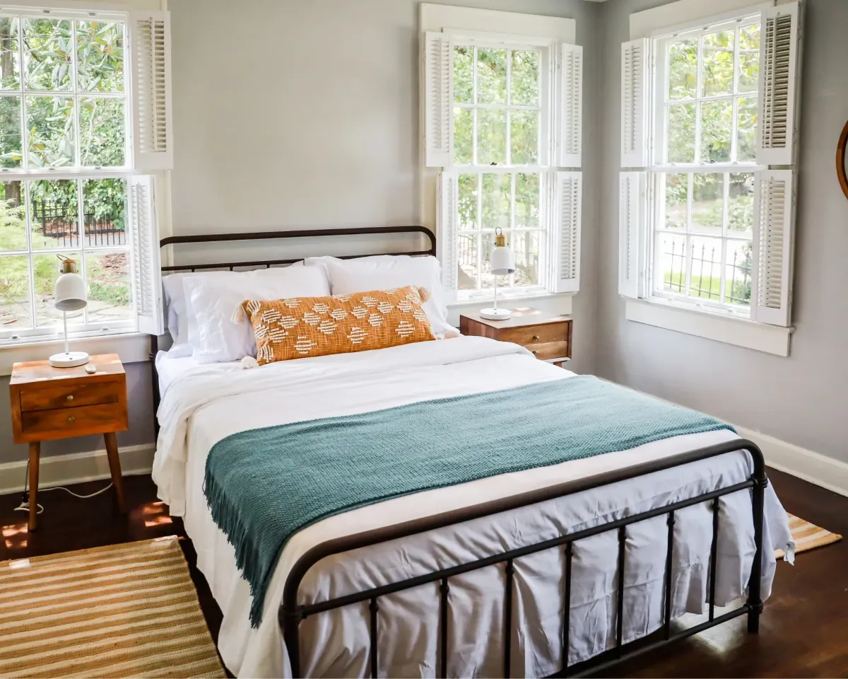 Cozy bedroom with a made bed, white bedding, teal throw, and wooden nightstands.