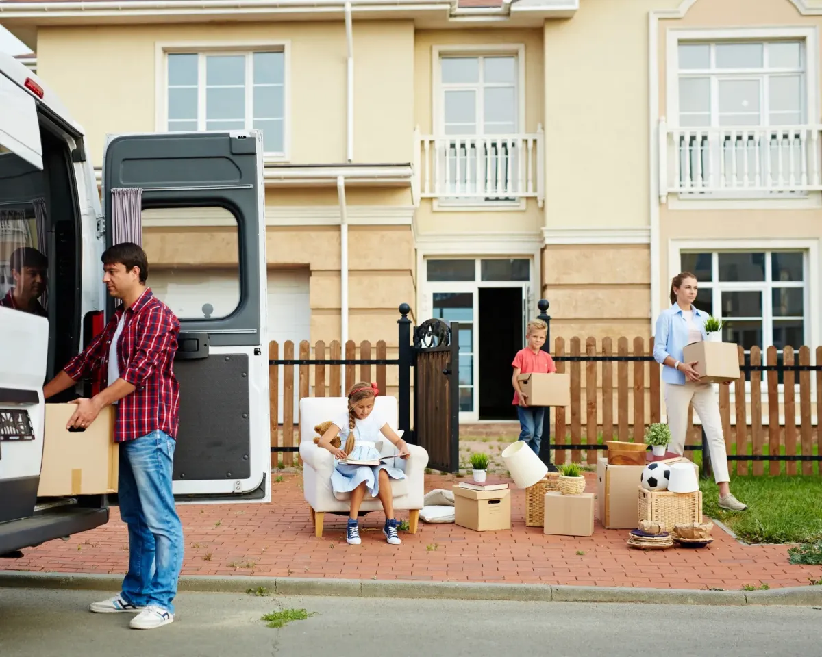 Family unpacking boxes from a van in front of a suburban house.