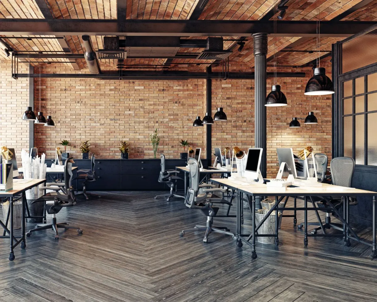 Modern office space with exposed brick walls, wooden beams, and computer desks.