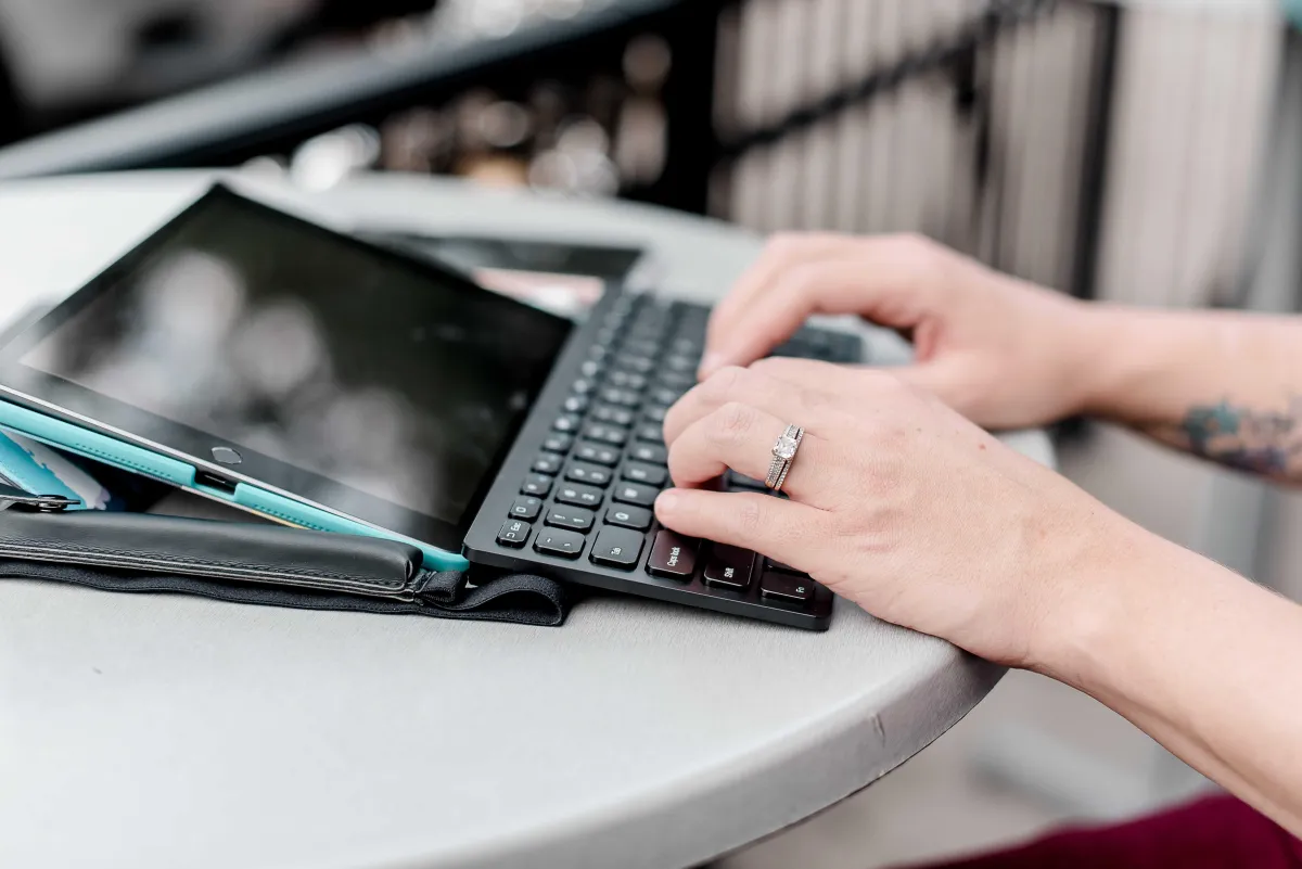 Close-up of hands typing on a keyboard with a tablet, showcasing the tech-savvy skills and dedication of mompreneurs