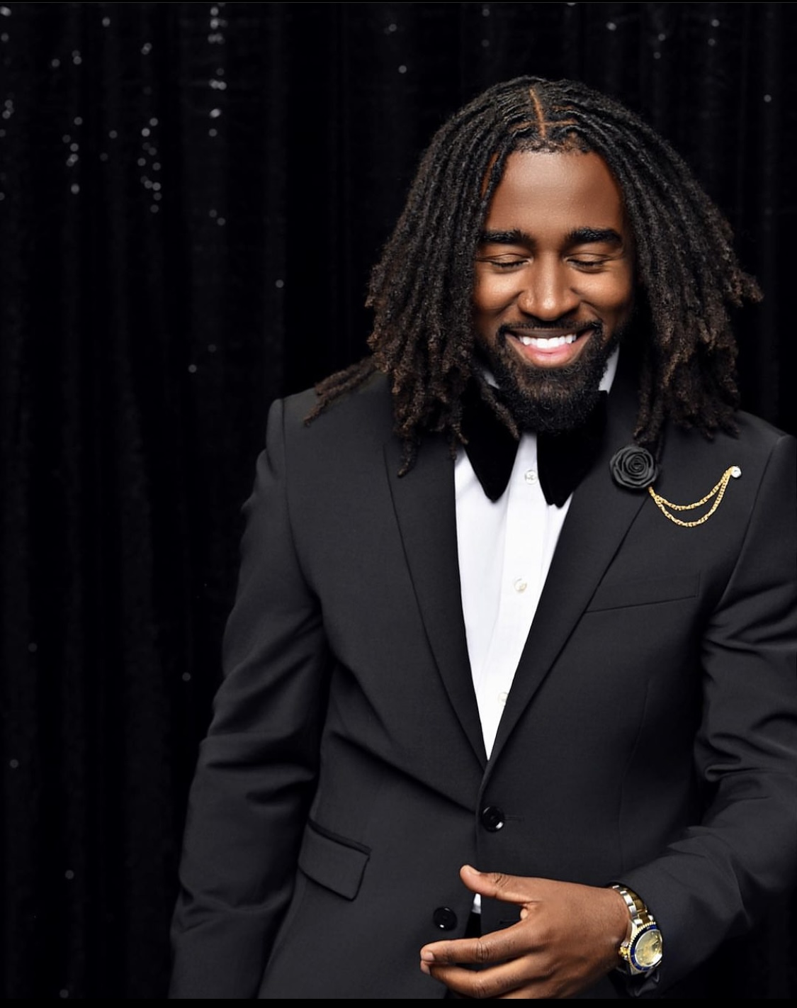 Man in a suit standing outdoors with cars behind him.