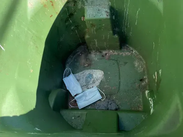 Dirty green trash bin with used masks and debris before cleaning