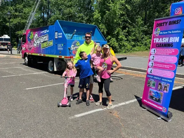Supreme Bins team with family at community event showcasing trash bin cleaning truck