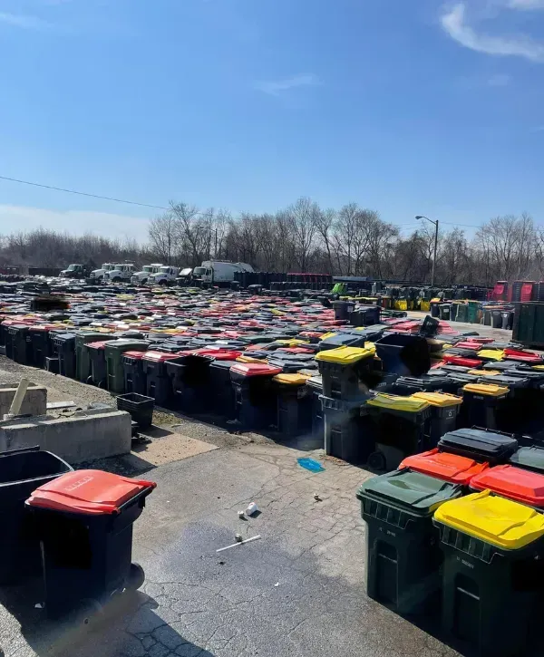 Hundreds of residential trash bins with red, yellow, and black lids in a storage yard