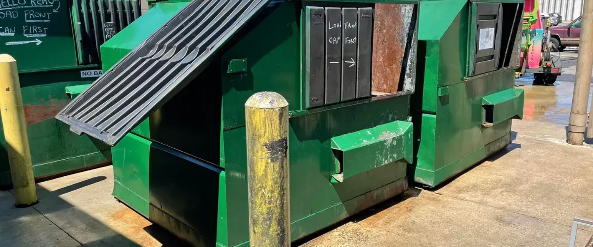 Two commercial green dumpsters before cleaning at a service area