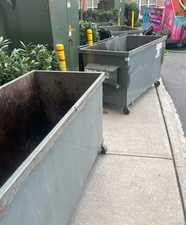 Large industrial dumpsters lined up on the sidewalk, ready for professional cleaning