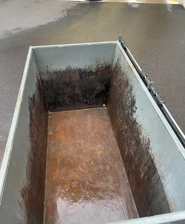 Interior of a dirty commercial dumpster showing rust, grime, and residue buildup.
