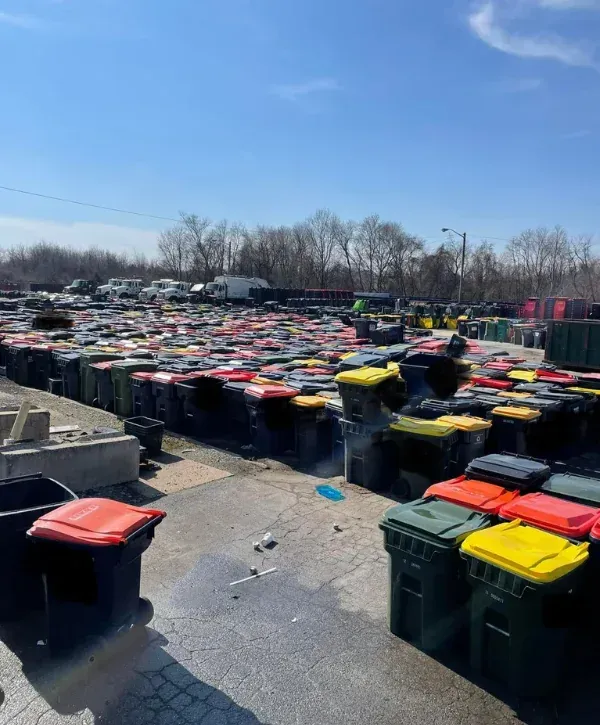 Large collection of commercial trash bins with colored lids at a sanitation facility, ready for cleaning and maintenance.