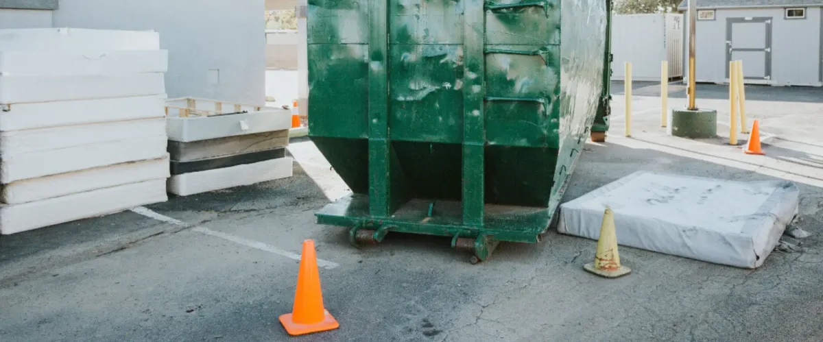Industrial green dumpster in loading area with construction materials nearby