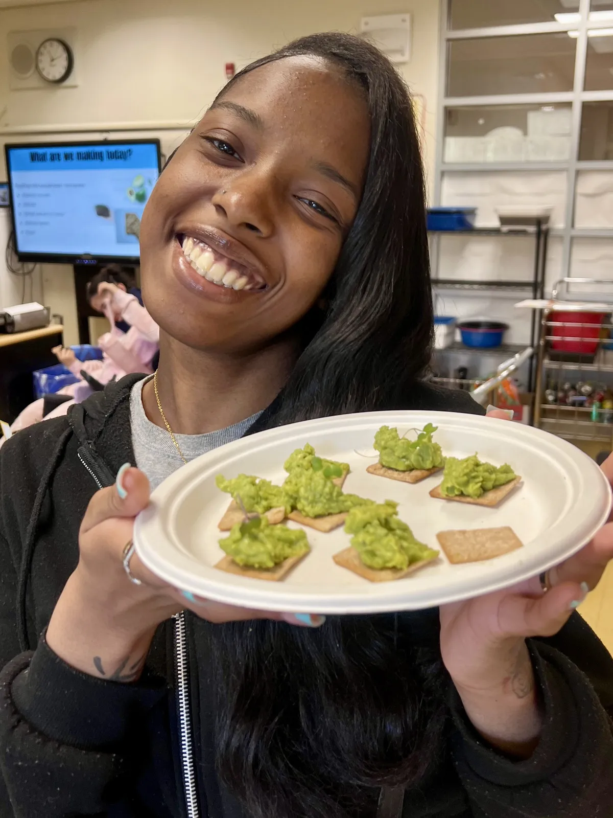 Smiling student holding a plate of homemade guacamole on crackers