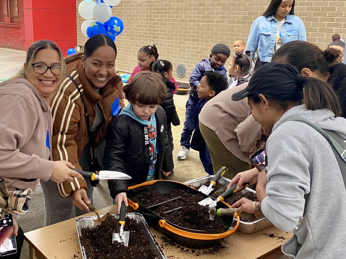 Parents and young children planting seeds in soil trays at an outdoor family gardening event