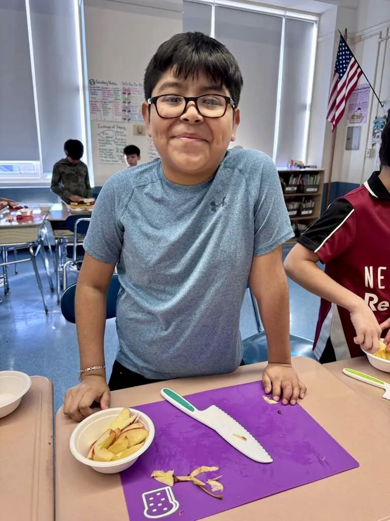 Student with a bowl of apple slices cut using a kid-safe knife on a cutting mat