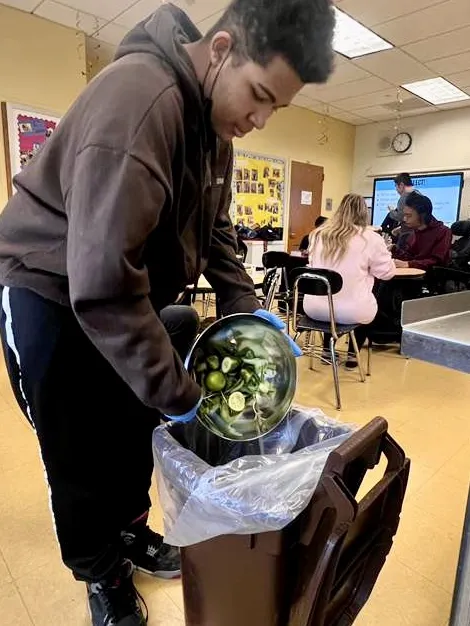 High school student emptying cucumber scraps into a classroom compost bin