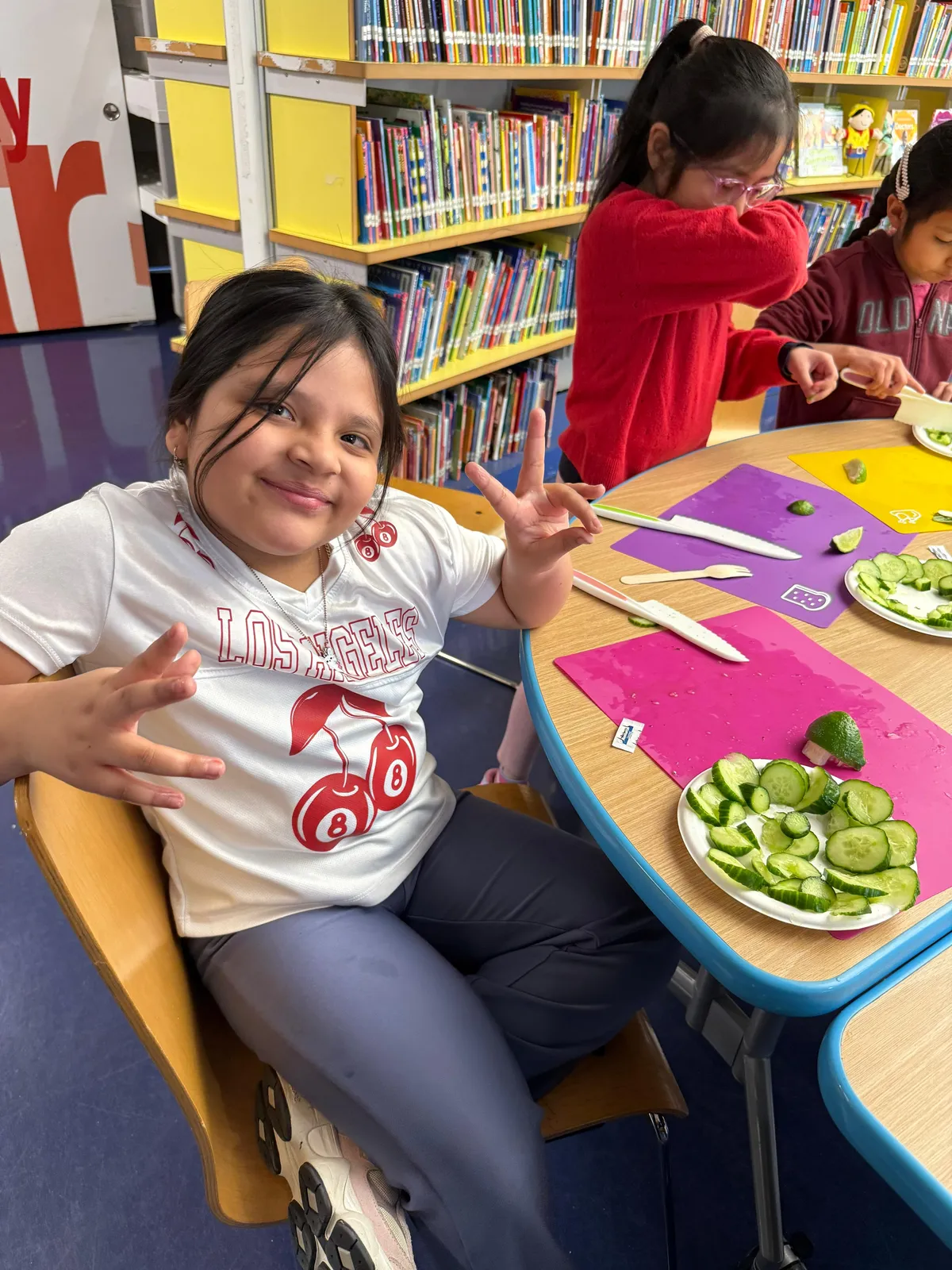 Student smiling at a library table with plates of sliced cucumber and lime during a food lesson