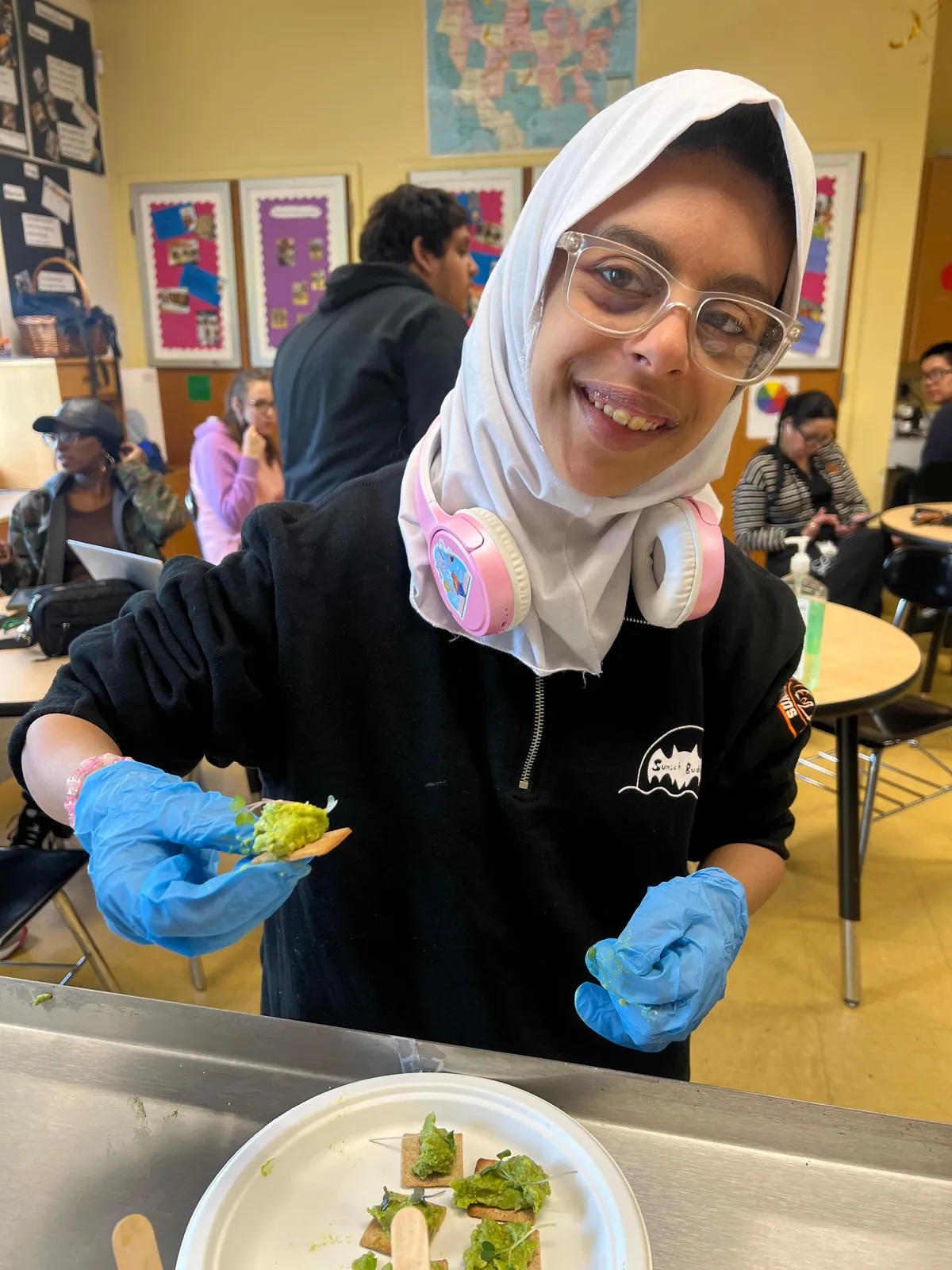 Student wearing gloves topping crackers with guacamole in a classroom kitchen
