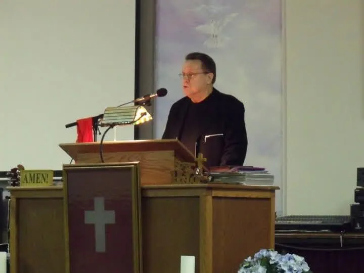 Pastor Richard Chronister preaching behind the wooden pulpit at Paradisus Church of God.