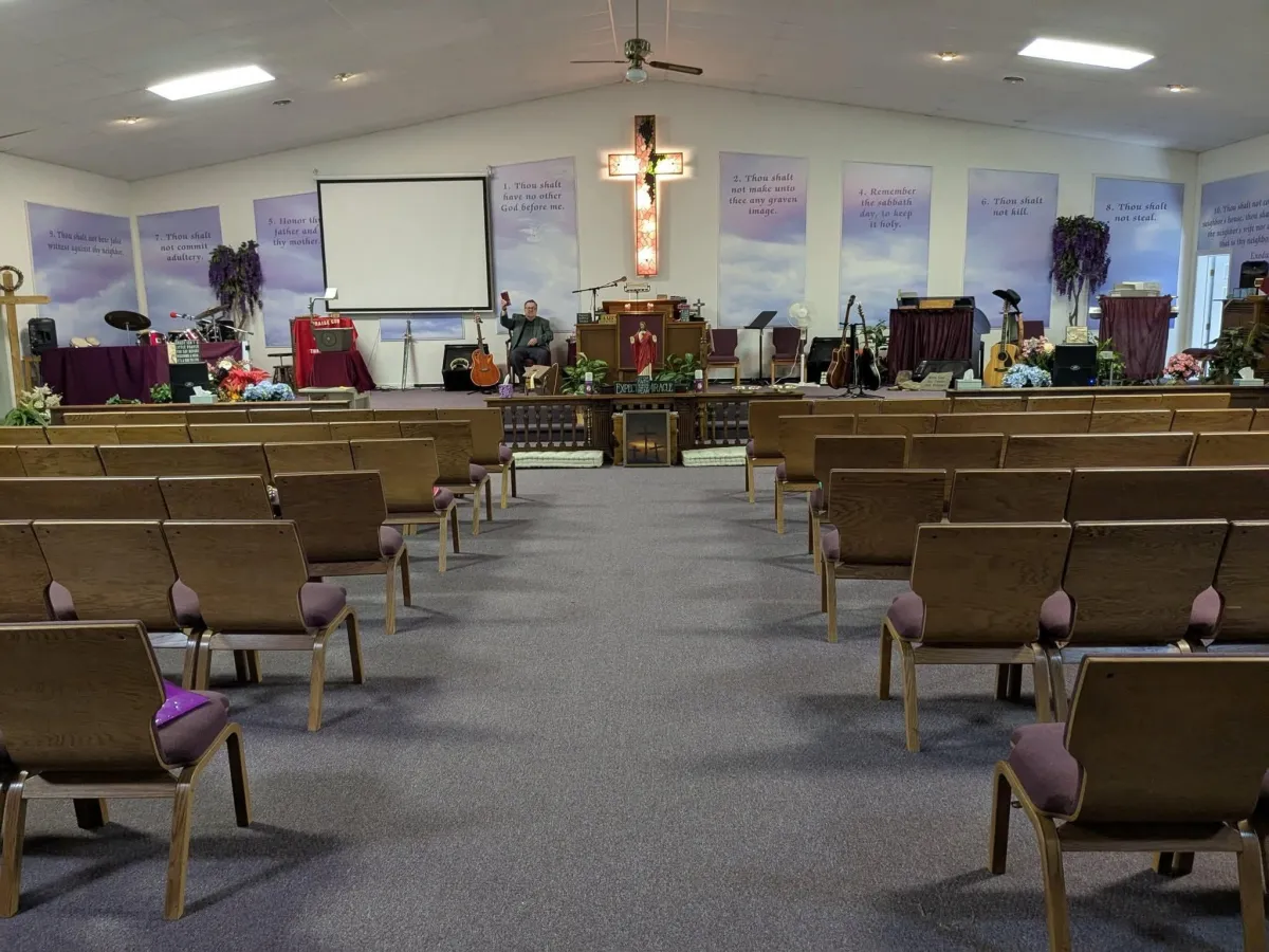 Paradisus Church of God sanctuary with rows of wooden chairs, purple accents, and an illuminated cross above the pulpit.