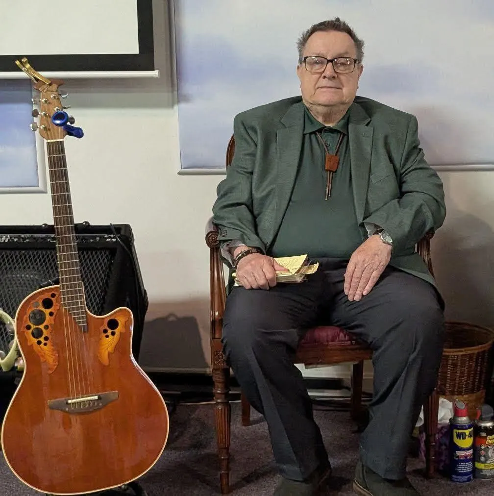 Pastor Richard Chronister seated beside an acoustic guitar in the sanctuary at Paradisus Church of God.