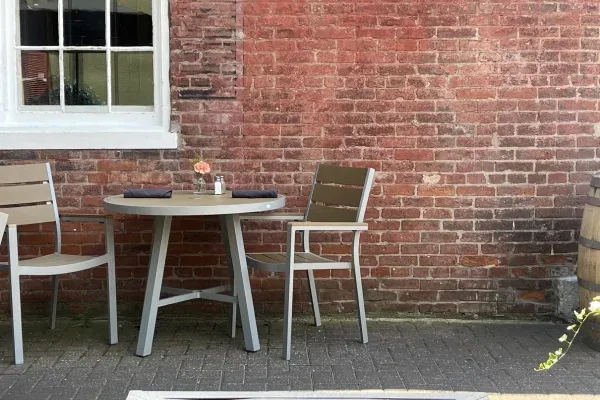 An outdoor dining table with two chairs sits on a paved patio against a weathered brick wall.