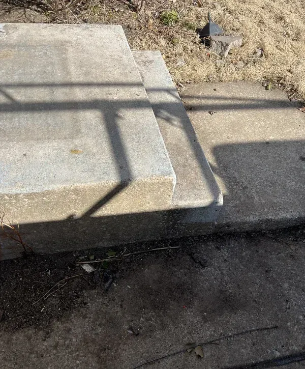 Concrete outdoor steps partially shaded by railing shadows, set against dry grass and dirt.