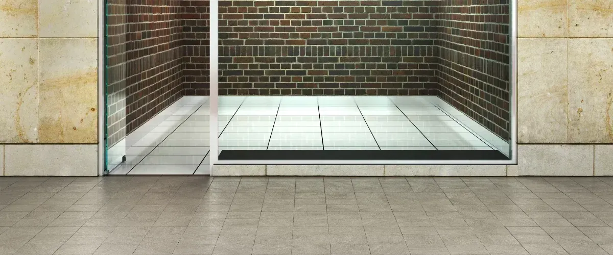 A modern walk-in shower with clear glass panels, white tiled floor, and a dark brick back wall.