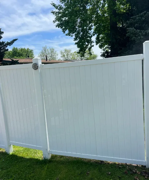 A clean white vinyl privacy fence with a small solar light on a post, against a backdrop of green trees and a blue sky.