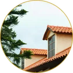 A completed orange clay tile roof with a dormer window beside green tree branches under a clear sky