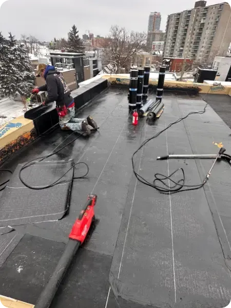 Worker installing flat commercial roofing membrane with torch tools on rooftop in Ottawa